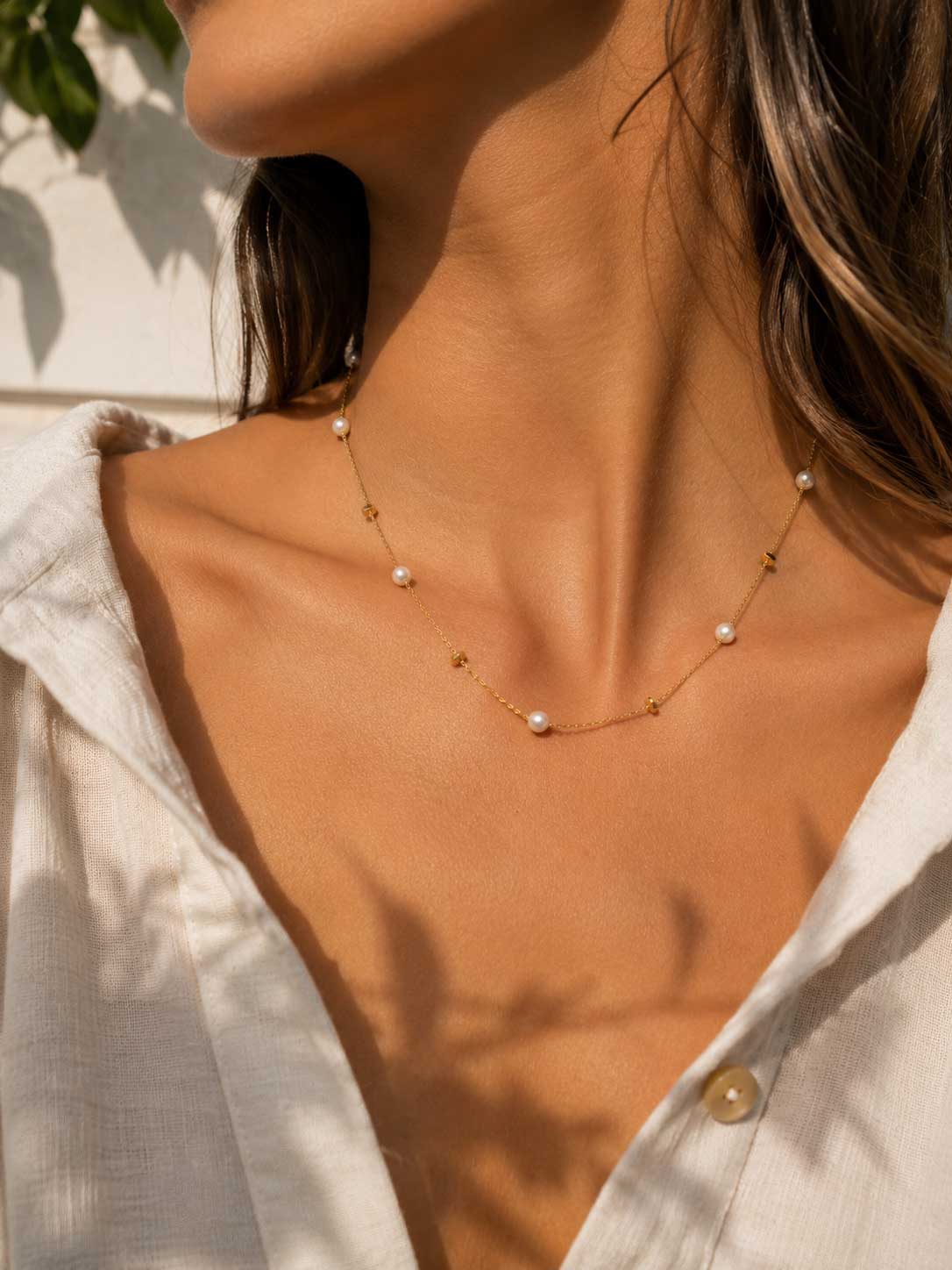 Golden Pearl Halskette Lifestyle – goldene Perlenkette von Saltyblush am Hals einer Frau, eleganter Look zu weißem Leinenhemd im Sonnenlicht, feminines Schmuckstück