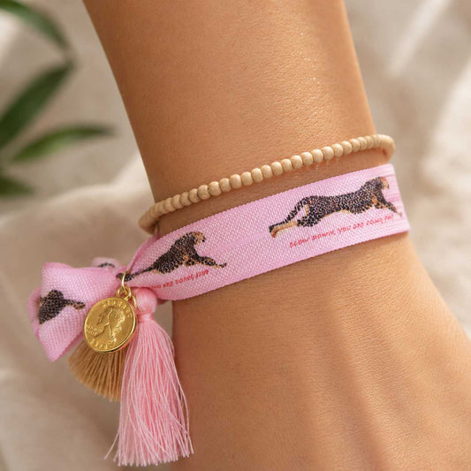 Elastisches Armband-Set Leopard in Rosa mit Leopard-Print-Band und beigem Holzperlenarmband am Handgelenk getragen – pinke Quaste mit goldenem Münzanhänger, Saltyblush