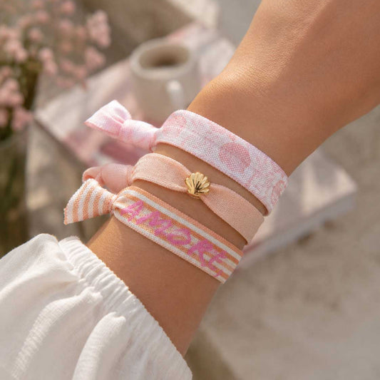 Elastisches 3er Armband-Set Soft Amore – rosa Kuss-Print-Band, pfirsichfarbenes Band mit goldenem Muschelanhänger und „Amore"-Streifenband kombiniert am Handgelenk – Saltyblush