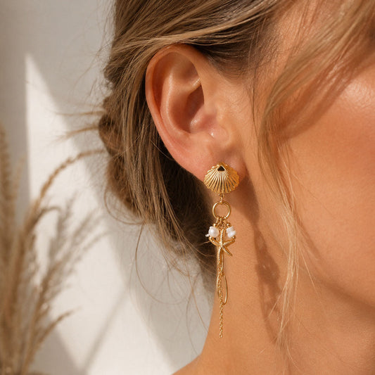 Goldene Muschel-Ohrringe Seashell Glow mit Seestern und Perlen am Ohr getragen – Saltyblush