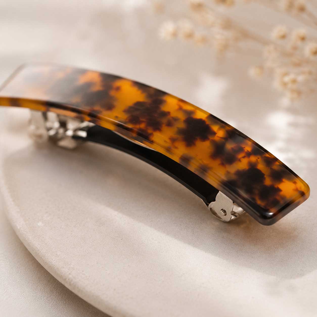 Nahaufnahme der Amber Curve Haarspange aus Acryl im Schildpatt-Design mit silbernem Metallverschluss auf weißem Tablett – Saltyblush