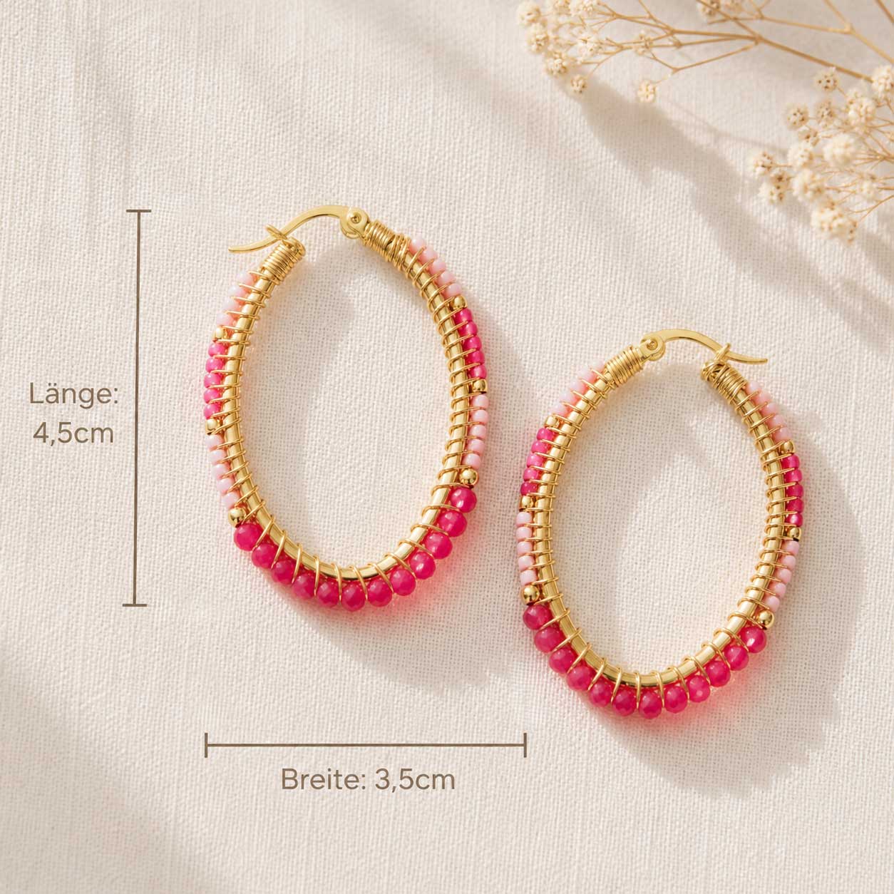 Goldene Perlen-Creolen Infografik – ovale Ohrringe mit pinken Kristallperlen, Länge 4,5 cm, Breite 3,5 cm mit Schleierkraut auf weißem Hintergrund