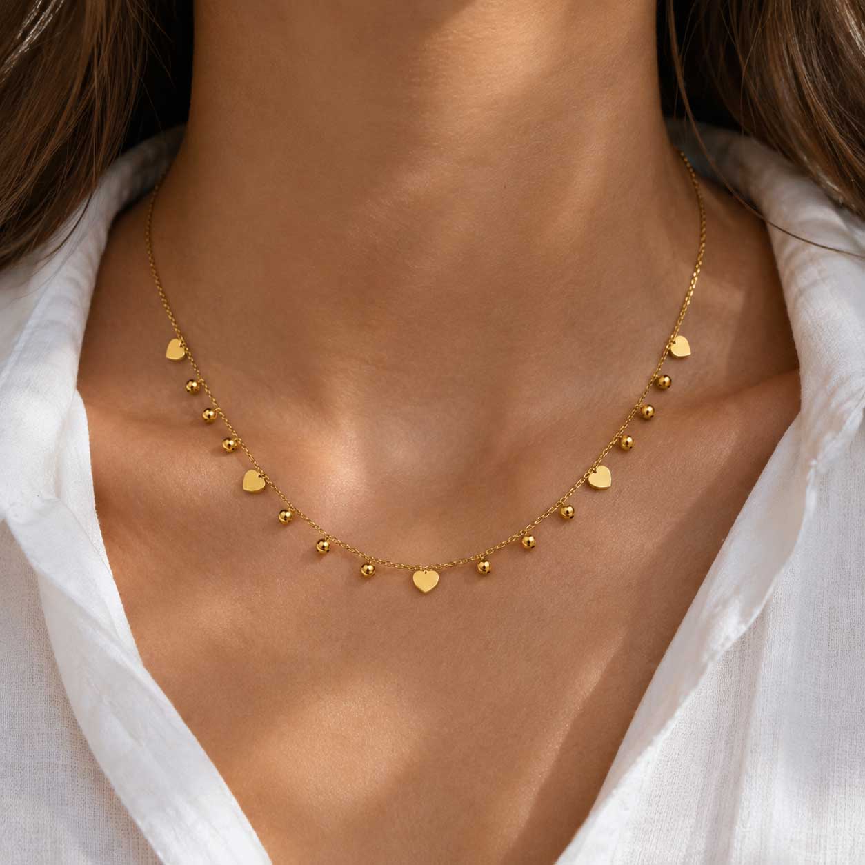Blushheart Halskette getragen – goldene Herz-Kugel-Halskette von Saltyblush am Hals einer Frau, eleganter Look zu weißem Hemd, feminines Schmuckstück