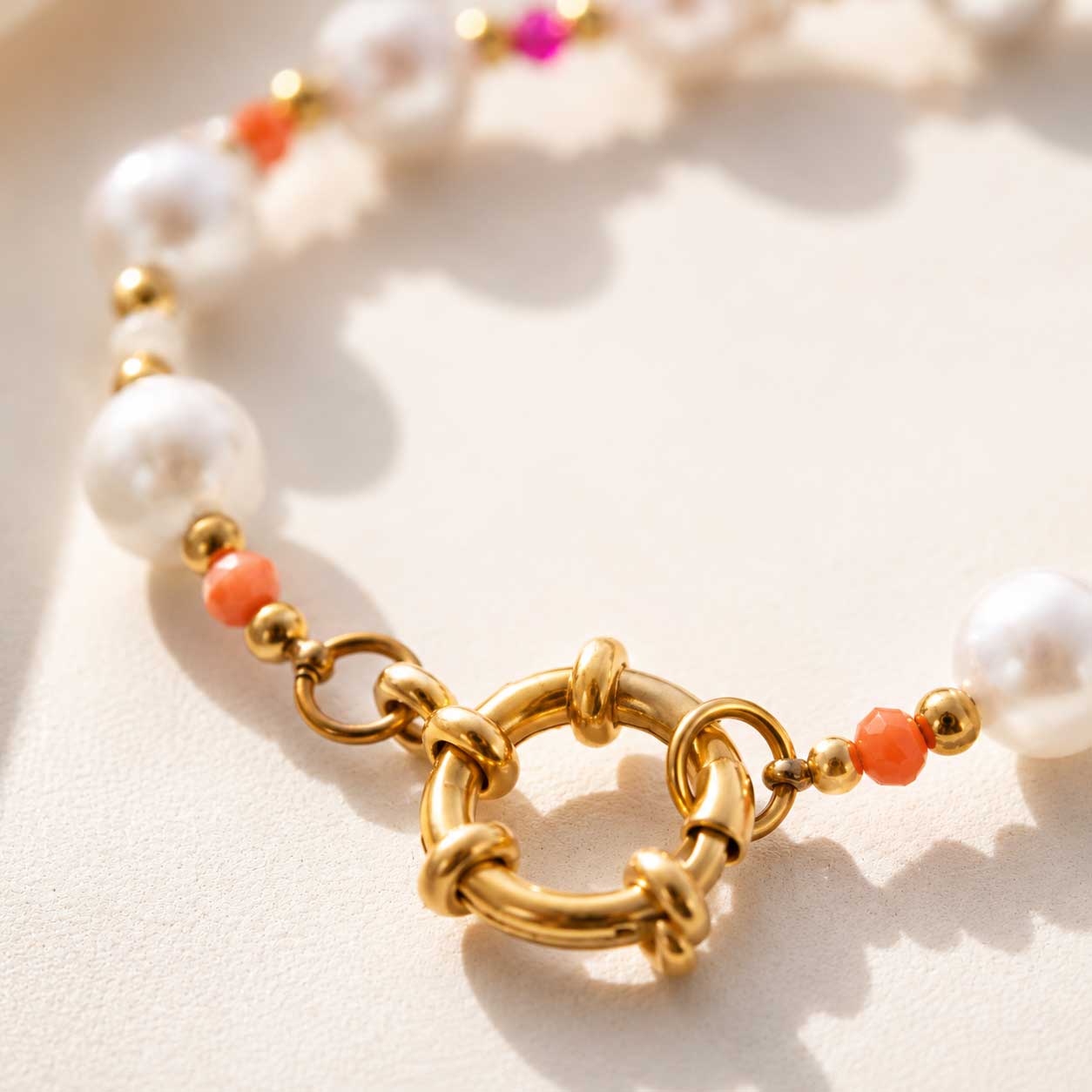 Nahaufnahme des goldenen Ringverschlusses am Candy Pearl Armband, Detailansicht des vergoldeten Edelstahl-Karabinerringes mit weißen Perlen und orangefarbenen Kristallen