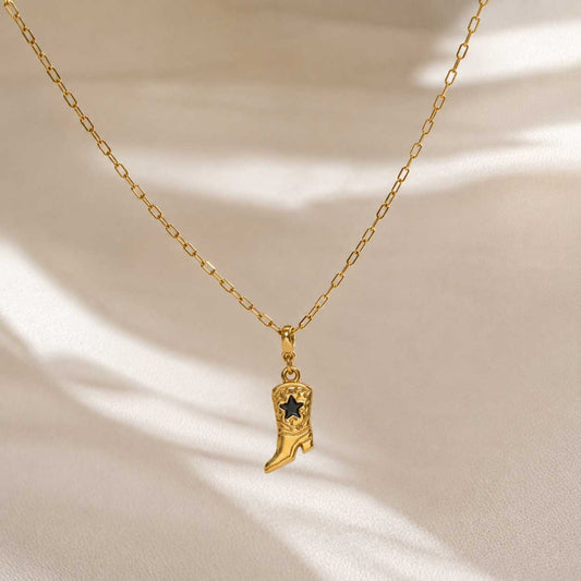 Goldene Gliederkette mit Cowboy Boot Charm in Gold-Schwarz auf cremefarbenem Hintergrund mit Lichtreflexen – Saltyblush