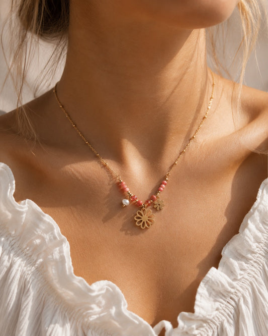 Goldene Flower Power Halskette am Hals getragen mit rosa Perlen, Süßwasserperle und zwei goldenen Blumen-Charms zu weißem Rüschenoberteil im Sonnenlicht, vergoldete Edelstahl-Satellitenkette