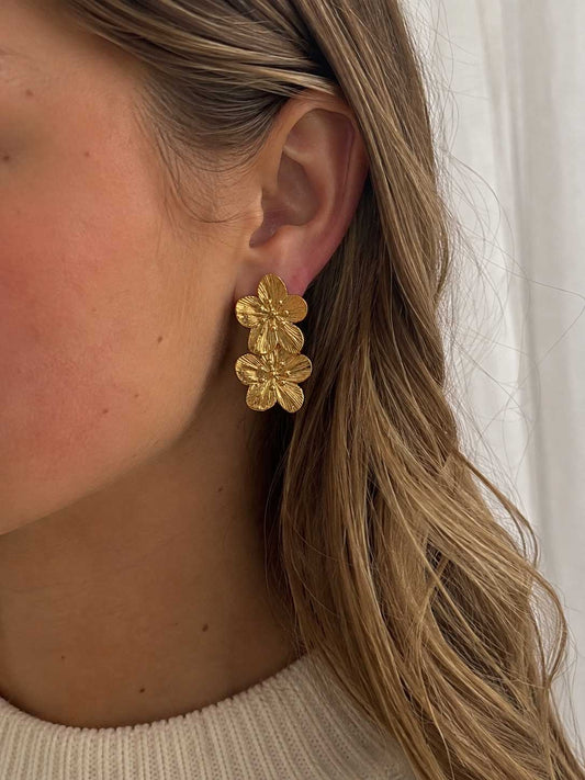 Frau mit langen blonden Haaren trägt die Golden Blossom Ohrringe mit doppeltem Blütendesign am Ohr – Saltyblush