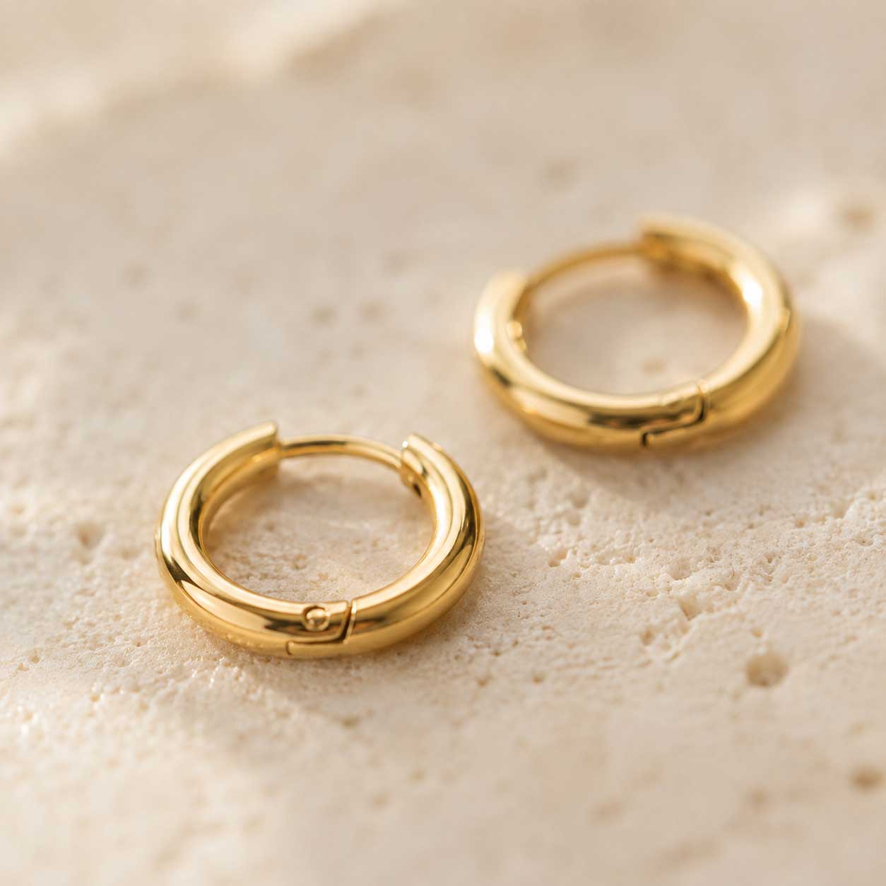 Nahaufnahme goldener Creolen aus Edelstahl auf Steinuntergrund – Detail des Klappverschlusses – Saltyblush