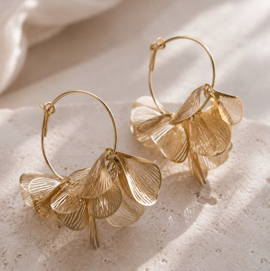 Goldene Creolen mit mehrlagigen Blütenblatt-Anhängern auf hellem Steinuntergrund – Golden Petal Hoops von Saltyblush