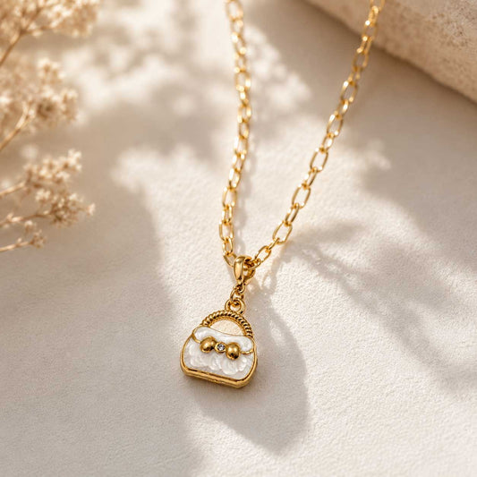 Goldene Halskette mit weißem Handtaschen-Charm an goldenem Gliederkette auf hellem Hintergrund mit Trockenblumen – Saltyblush