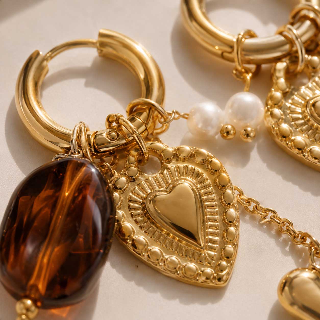 Detailaufnahme goldene Creolen heartbeat – Herz-Charm mit Gravur, braune Bernsteinperle und Süßwasserperle | Saltyblush