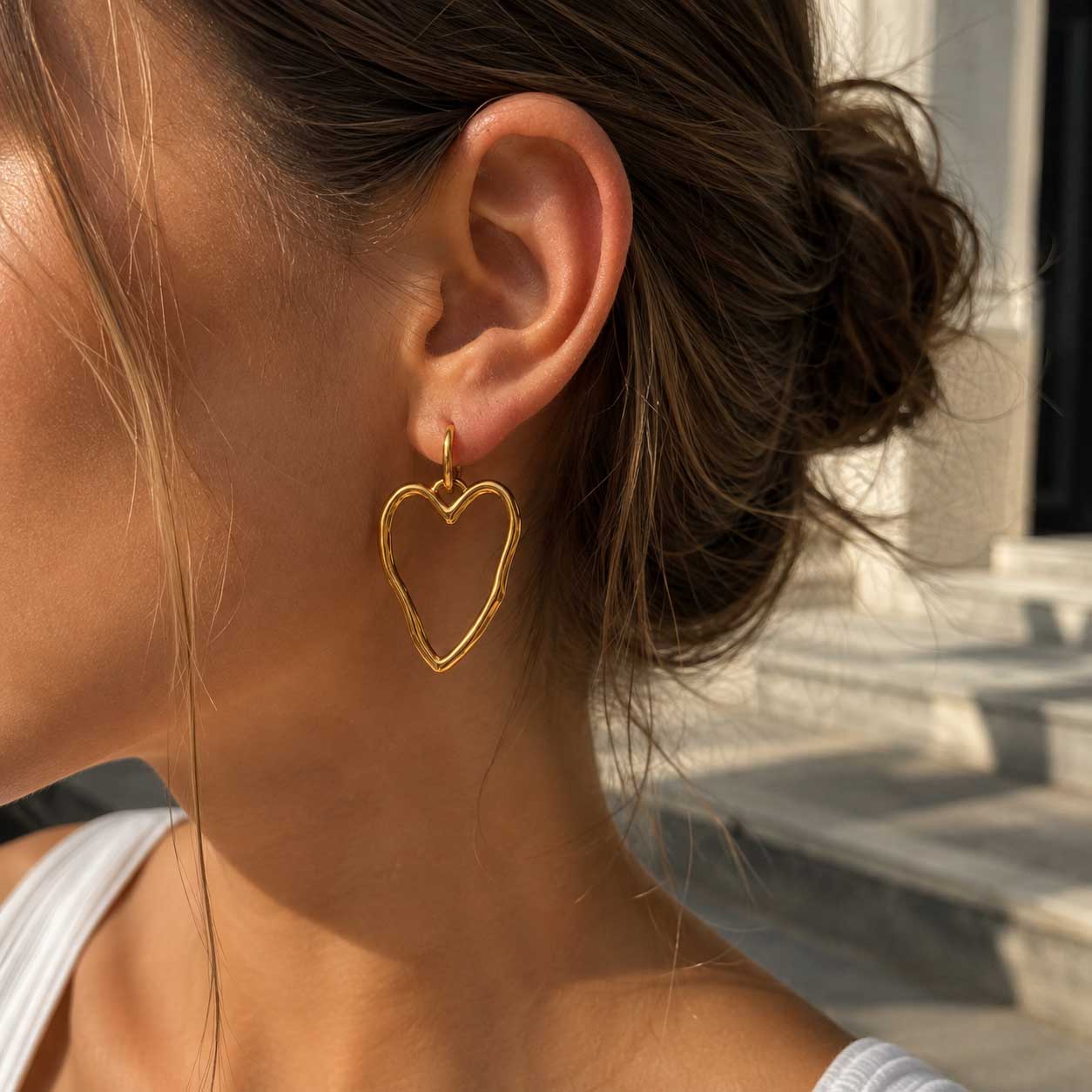 Frau mit braunem Dutt trägt die Heartline goldenen Herz-Ohrringe aus Edelstahl im Sonnenlicht – Saltyblush