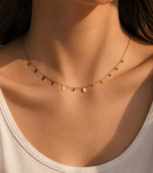 Minimalist Chic Halskette getragen – goldene Plättchen-Halskette von Saltyblush am Hals einer Frau, dezente Charms im Sonnenlicht, zu weißem Top