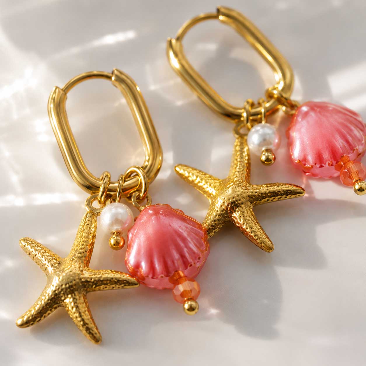 Detailaufnahme pearl and sea Ohrringe – goldener Seestern, rosa Muschel und Perle auf Perlmutt-Hintergrund