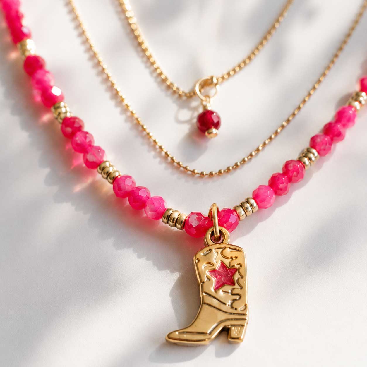 Nahaufnahme des goldenen Cowboy-Boot-Charms mit pinkem Stern an pinker Perlenkette aus Edelstahl – Saltyblush