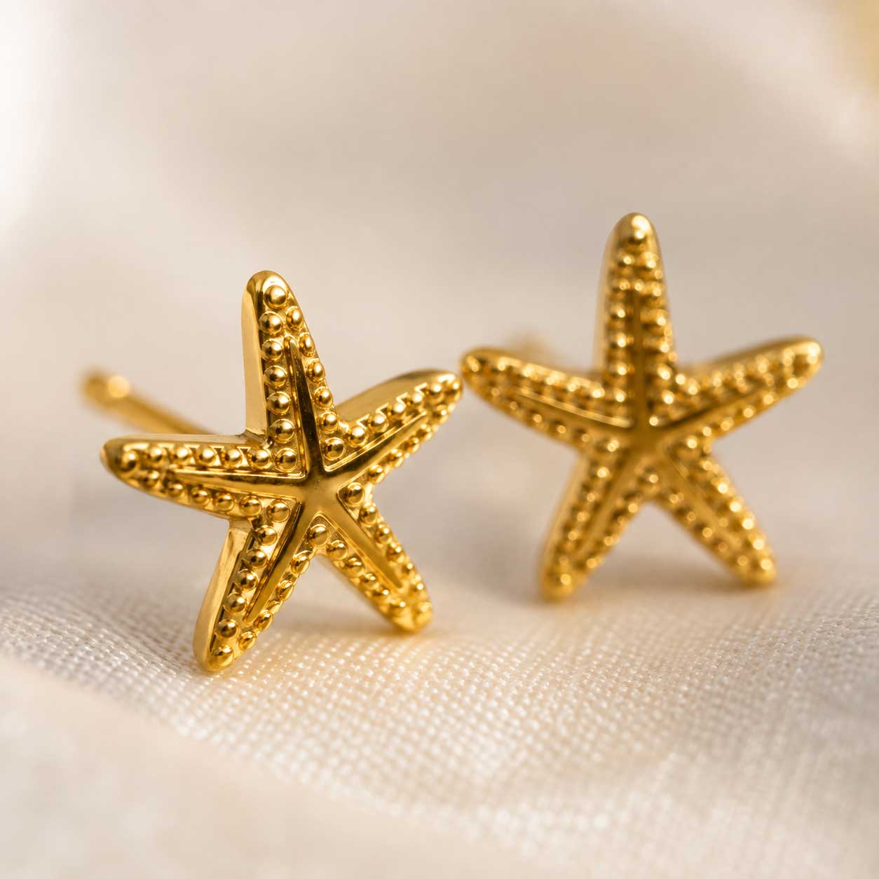 Nahaufnahme goldene Seestern Stecker – Sea Spirit Ohrringe von Saltyblush, detaillierte Oberflächenstruktur mit Kugelrand, Detailansicht auf weißem Stoff