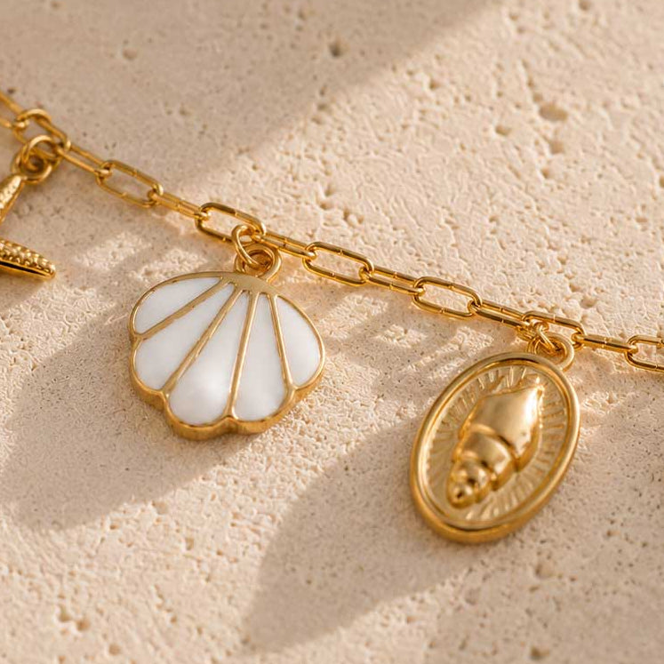 Nahaufnahme des weißen Muschel-Charms und goldenen Schnecken-Medaillons der Sea Whisper Fußkette aus Edelstahl – Saltyblush