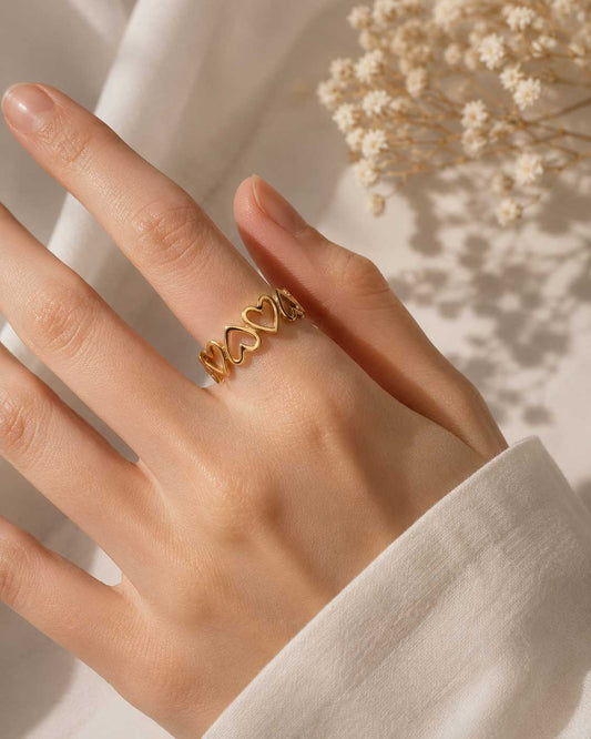 Goldener Herzring am Finger getragen, größenverstellbarer Ring mit Herz-Muster und Schleierkraut im Hintergrund