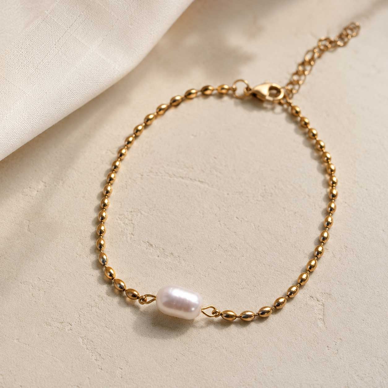 Goldenes Armband Pearl Tide mit weißer Perle und Kugelkette auf cremefarbenem Untergrund – Detailaufnahme, Saltyblush
