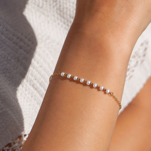 Goldenes Perlenarmband Pearl Whisper mit kleinen weißen Perlen am Handgelenk getragen – Saltyblush
