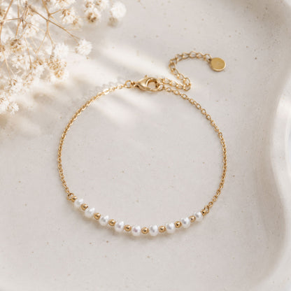 Goldenes Perlenarmband Pearl Whisper mit feiner Goldkette auf cremefarbener Schale – Saltyblush
