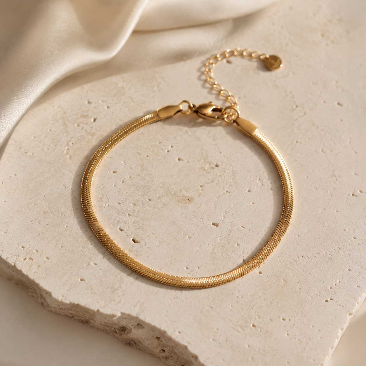 Goldenes Edelstahl-Armband Silk Chain auf beigem Travertin-Stein – Saltyblush
