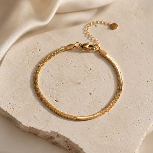 Goldenes Edelstahl-Armband Silk Chain auf beigem Travertin-Stein – Saltyblush
