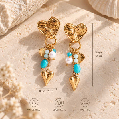 Goldene salty heart Ohrringe mit Herz- und Perlenanhängern. Maßangaben: 6,5 cm Länge und 2 cm Breite; Bildhinweise zu Edelstahl, Wasserfestigkeit und Rostfreiheit.
