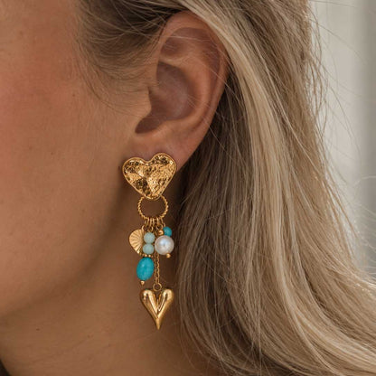 Goldener salty heart Ohrring am Ohr bei offenem blondem Haar, mit strukturiertem Herzstecker, türkisfarbenen und mintgrünen Perlen, weißer Perle und hängendem Goldherz.
[AI]