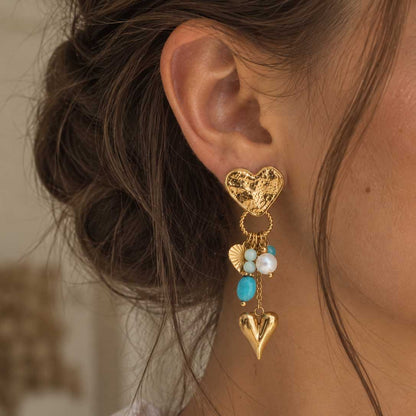 Goldener salty heart Ohrring am Ohr bei locker hochgestecktem braunem Haar, mit strukturiertem Herzstecker, türkisfarbenen, mintgrünen und weißen Perlen sowie goldenem Herzanhänger.
[AI]