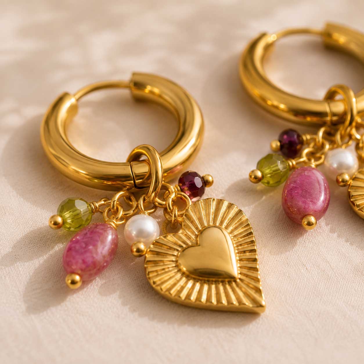 Nahaufnahme goldene Creolen Dolce Cuore mit graviertem Herz-Charm, pinken Steinen, Perle & grünen Kristallen – Edelstahl – Saltyblush
