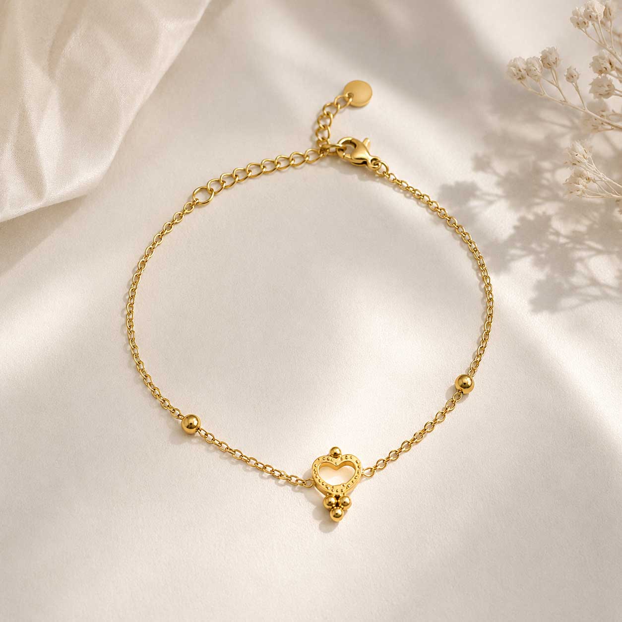 Nahaufnahme goldenes Herzarmband – Golden Glow Armband von Saltyblush, offener Herzanhänger mit Kugeldetails an feiner Satellitenkette, Detailansicht auf grauem Untergrund
