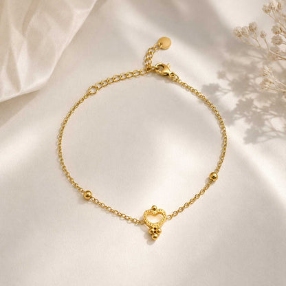 Nahaufnahme goldenes Herzarmband – Golden Glow Armband von Saltyblush, offener Herzanhänger mit Kugeldetails an feiner Satellitenkette, Detailansicht auf grauem Untergrund
