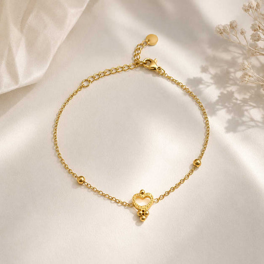 Nahaufnahme goldenes Herzarmband – Golden Glow Armband von Saltyblush, offener Herzanhänger mit Kugeldetails an feiner Satellitenkette, Detailansicht auf grauem Untergrund
