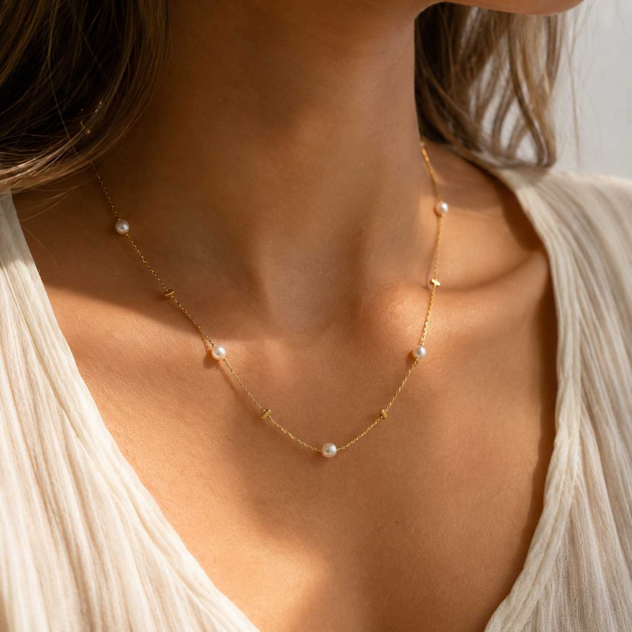 Golden Pearl Halskette getragen – goldene Perlenkette von Saltyblush am Hals einer Frau, zarte weiße Perlen auf feiner Goldkette, zu weißem Oberteil im Sonnenlicht
