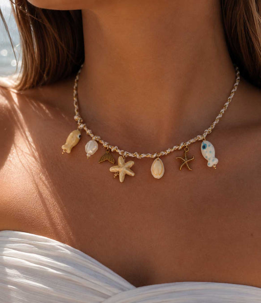 Salty Star Halskette getragen – maritime Charm-Kette von Saltyblush am Hals einer Frau, Seestern, Muschel, Fisch und Perlen-Charms zu weißem Bandeau-Top am Meer
