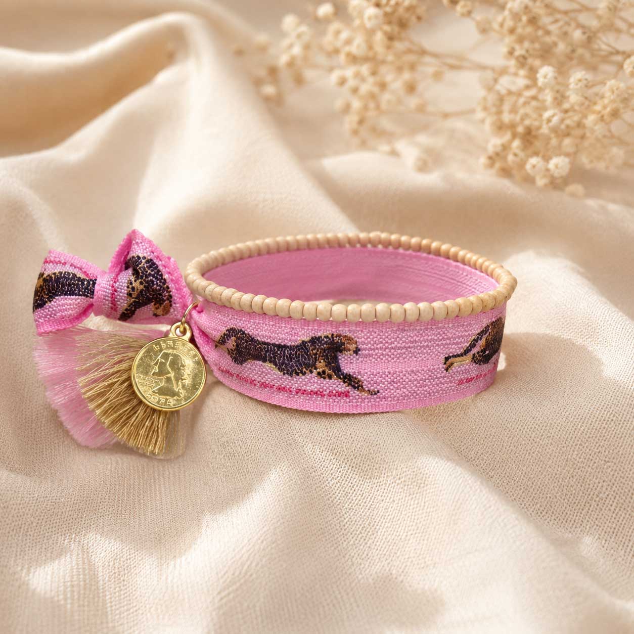 Elastisches Armband-Set Leopard in Rosa mit Leopard-Print-Band, pinker Quaste, goldenem Münzanhänger und beigem Holzperlenarmband auf cremefarbenem Seidenstoff – Saltyblush
