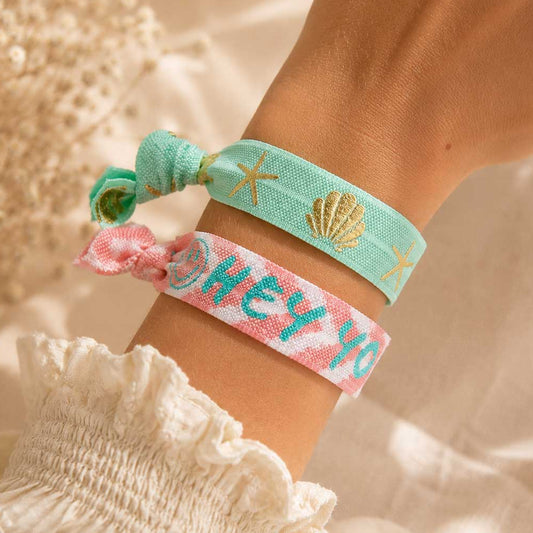 Elastisches Armband-Set Ocean Breeze mit mintgrünem Muschel-Band und rosa „HEY YOU,SMILE"-Band am Handgelenk getragen – Saltyblush
