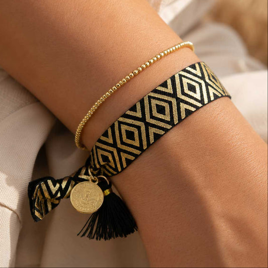 Elastisches Armband-Set Black & Gold mit schwarzem Rautenmuster-Band und goldenem Perlenarmband am Handgelenk getragen – schwarze Quaste mit goldenem Münzanhänger, Saltyblush

