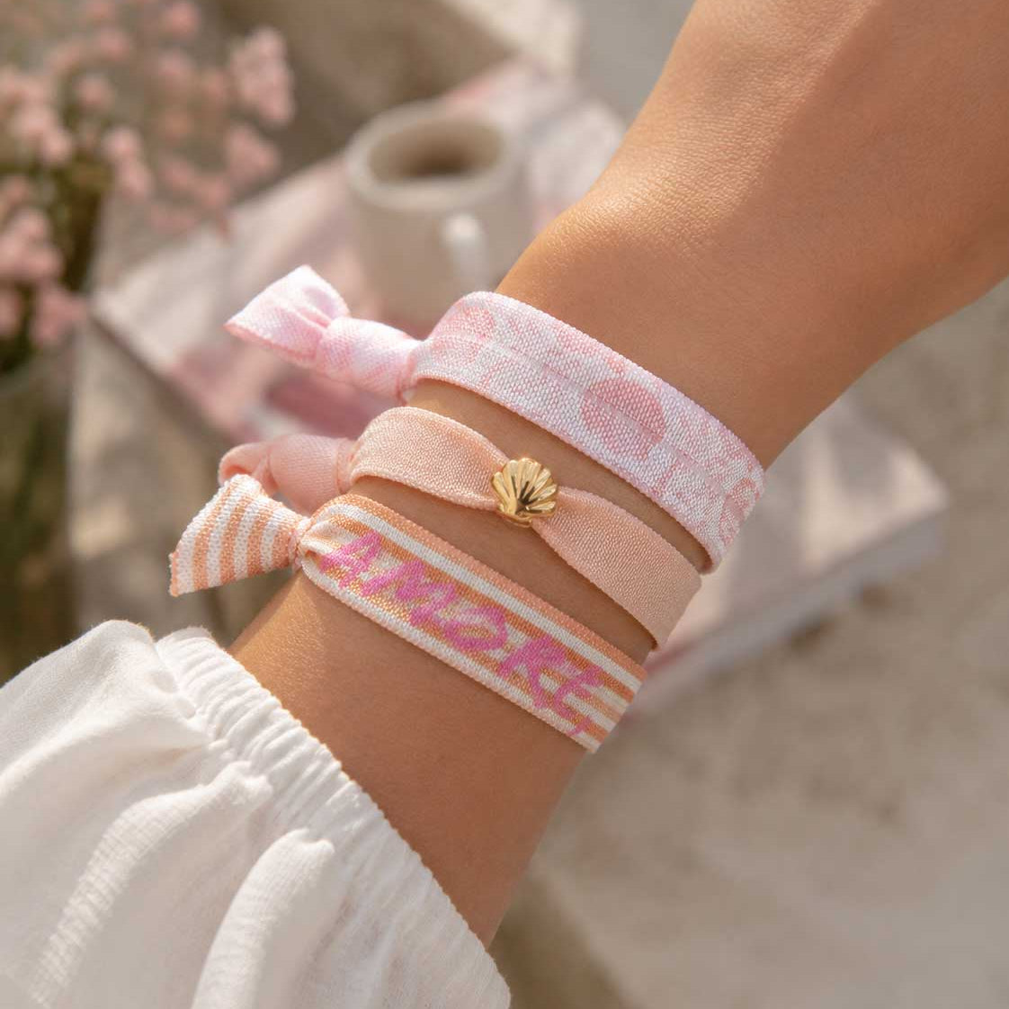 Elastisches 3er Armband-Set Soft Amore – rosa Kuss-Print-Band, pfirsichfarbenes Band mit goldenem Muschelanhänger und „Amore"-Streifenband kombiniert am Handgelenk – Saltyblush
