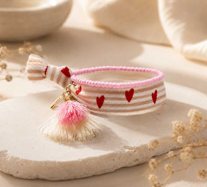 Elastisches Armband-Set Sweet Hearts mit Herz-Streifenband, rosa und cremefarbener Quaste und goldenem Anhänger auf Steinuntergrund – Saltyblush
