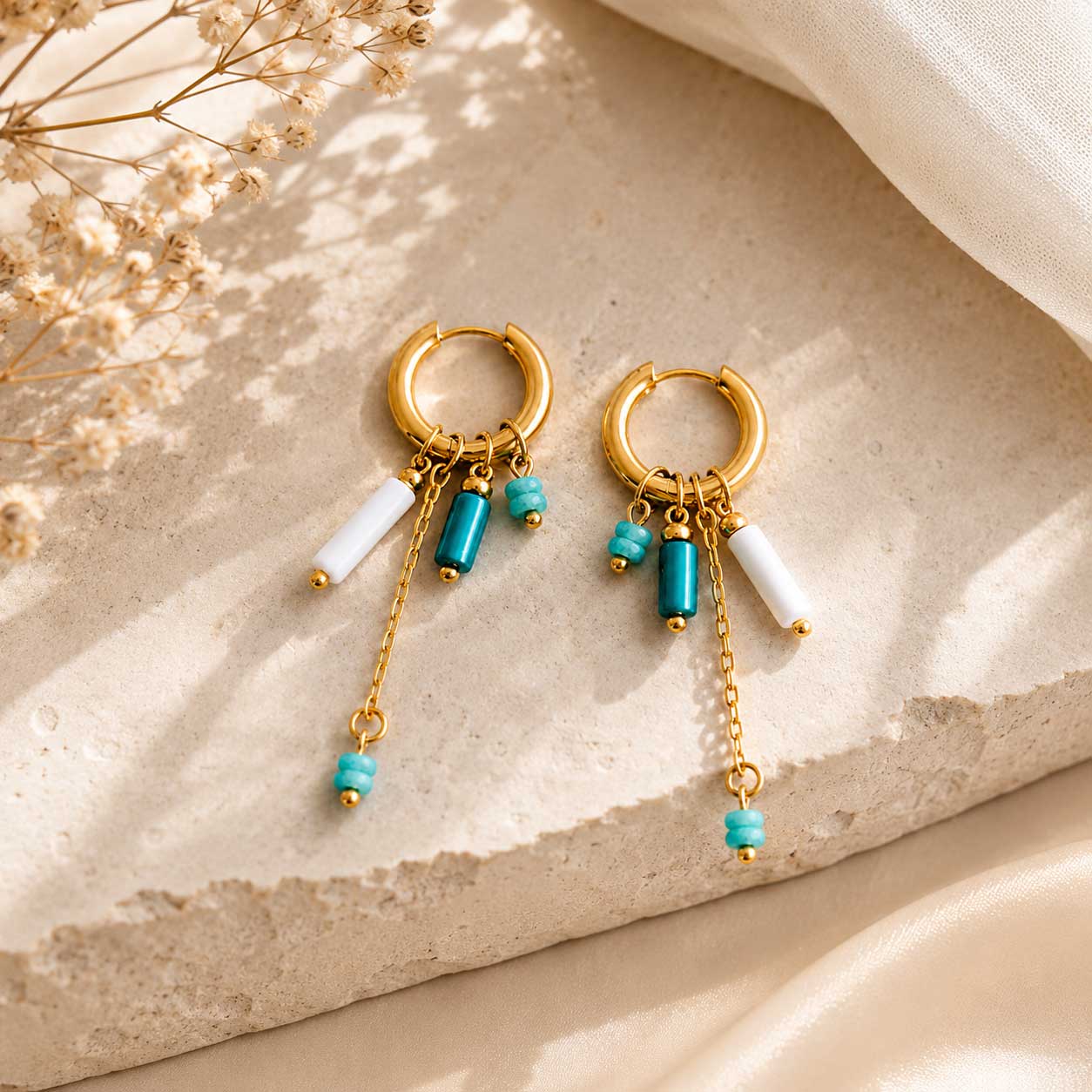 Goldene Creolen Blue Tide mit türkisen und weißen Perlen auf beigem Stein – Saltyblush
