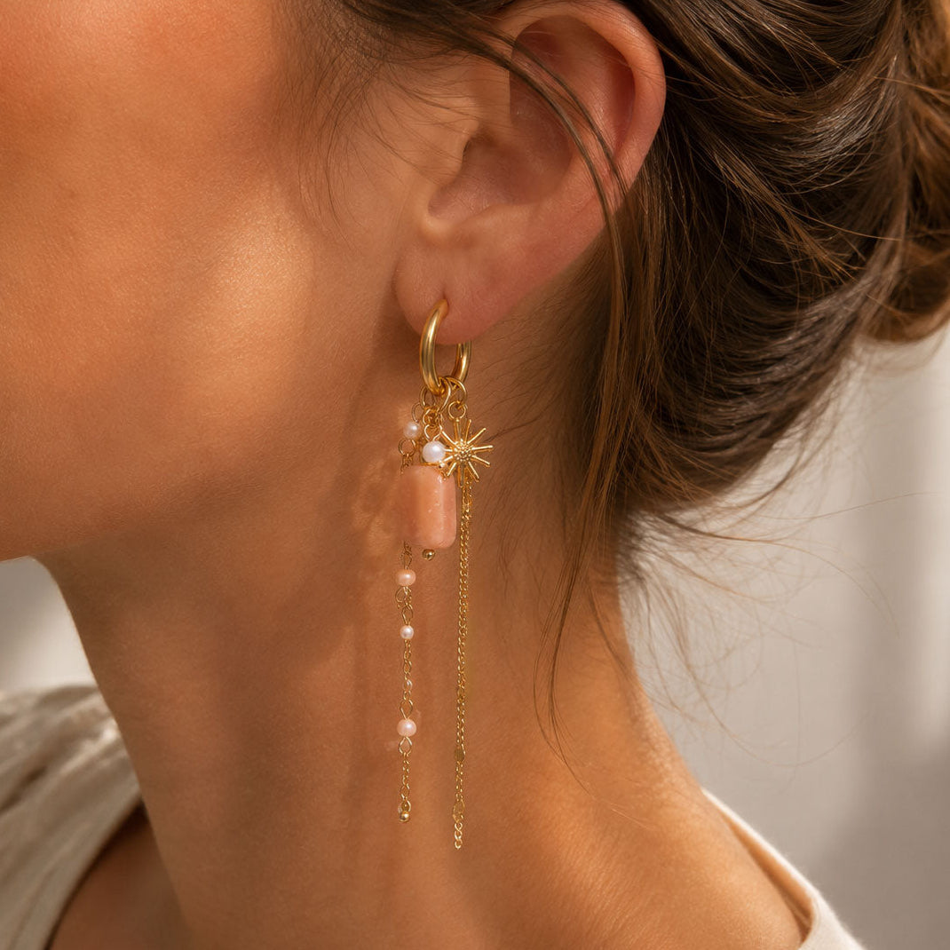 Goldene Statement-Ohrringe Rosé Ray mit Sonnenstern, rosafarbenem Stein und Goldketten am Ohr – Saltyblush
