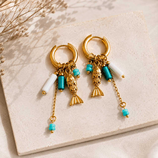 Goldene Creolen Seabreeze mit Fisch-Charm und türkisen Perlen auf beigem Stein – Saltyblush
