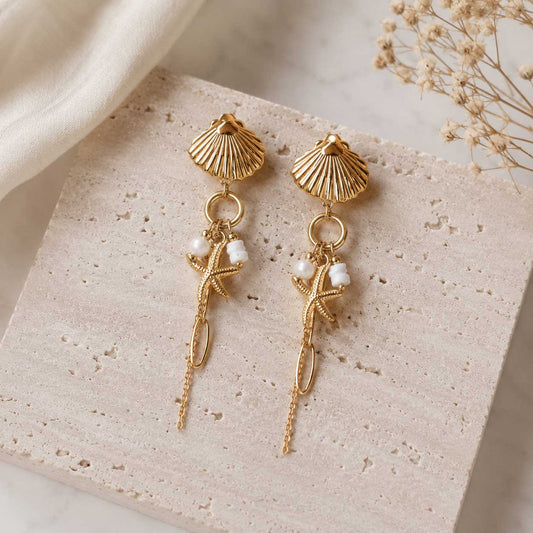 Goldene Muschel-Ohrringe Seashell Glow mit Seestern, Perlen und Goldkette auf beigem Stein – Saltyblush
