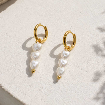 Goldene Creolen Amora mit drei herzförmigen weißen Perlen-Anhängern auf Travertinstein mit Sonnenschatten – Edelstahl, Saltyblush
