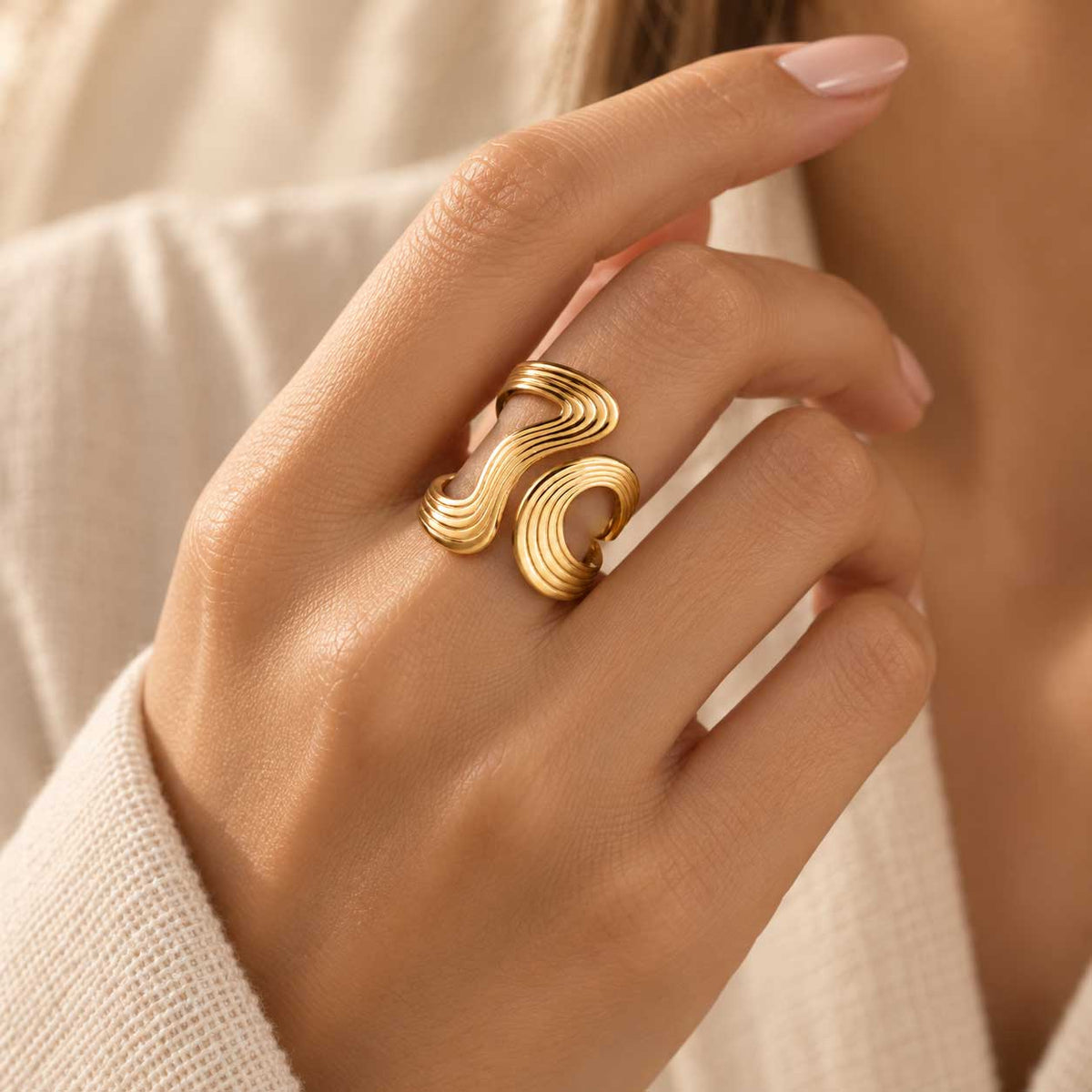 Goldener XL Swirl Statement-Ring aus Edelstahl an der Hand getragen, mit markanter Streifenoptik und auffälligem Design für Alltag und Abend
[AI]