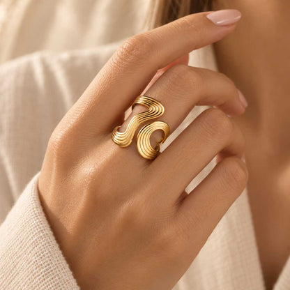 Goldener XL Swirl Statement-Ring aus Edelstahl an der Hand getragen, mit markanter Streifenoptik und auffälligem Design für Alltag und Abend
[AI]
