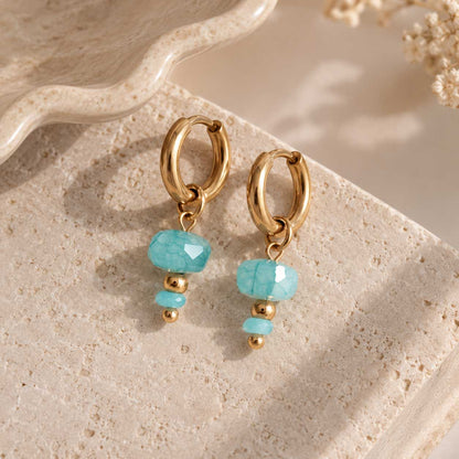 Goldene Edelstahl-Creolen mit facettierter Oberfläche und einem einzelnen aqua-blauen Drop-Charm, als Paar mit praktischem Klickverschluss
