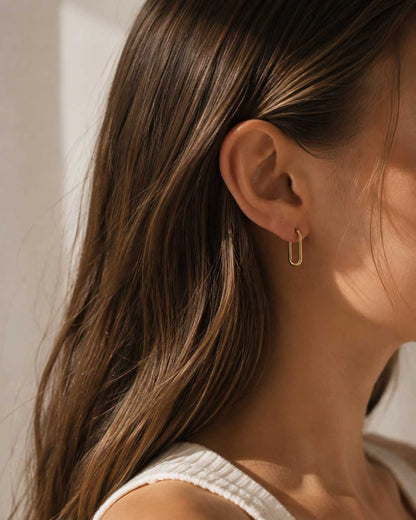 Bare Glow goldene Ohrringe in rechteckiger Form am Ohr getragen mit weißem Top im Sonnenlicht – Saltyblush
